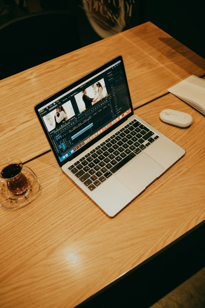 Un laptop su un tavolo di legno in una caffetteria, con software di montaggio video aperto per attività creative.